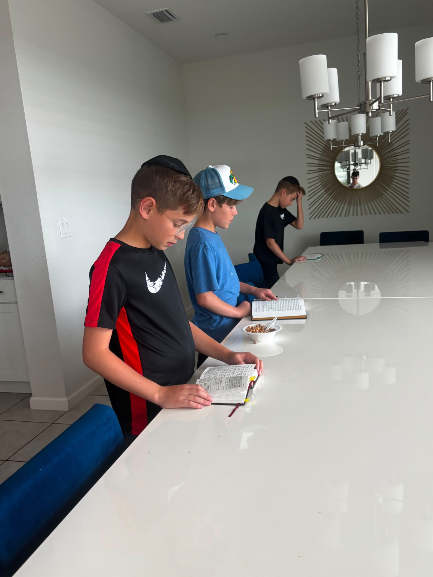 Three boys reading together from open prayer books at a long table