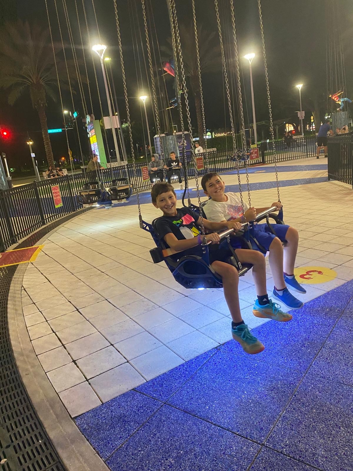 Two campers smiling on a swing ride at night