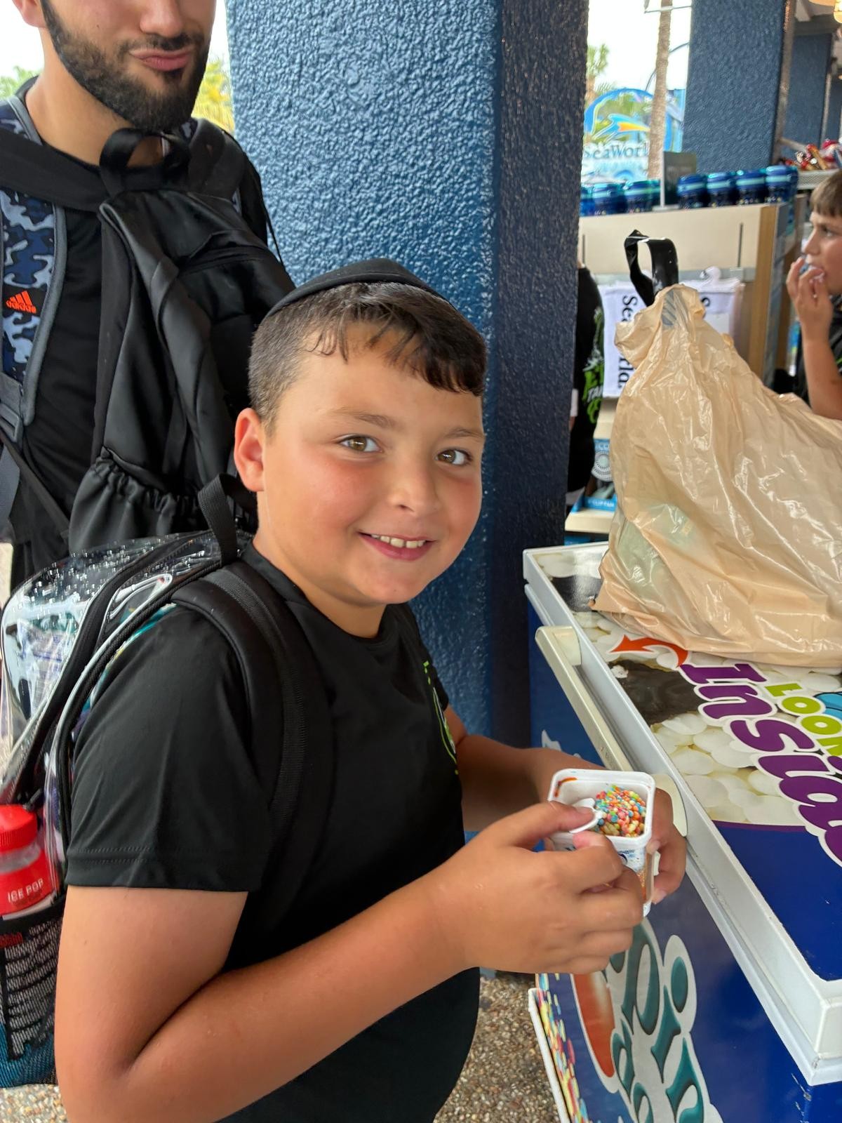 A smiling camper holding a cup of Dippin' Dots near a shop counter at SeaWorld