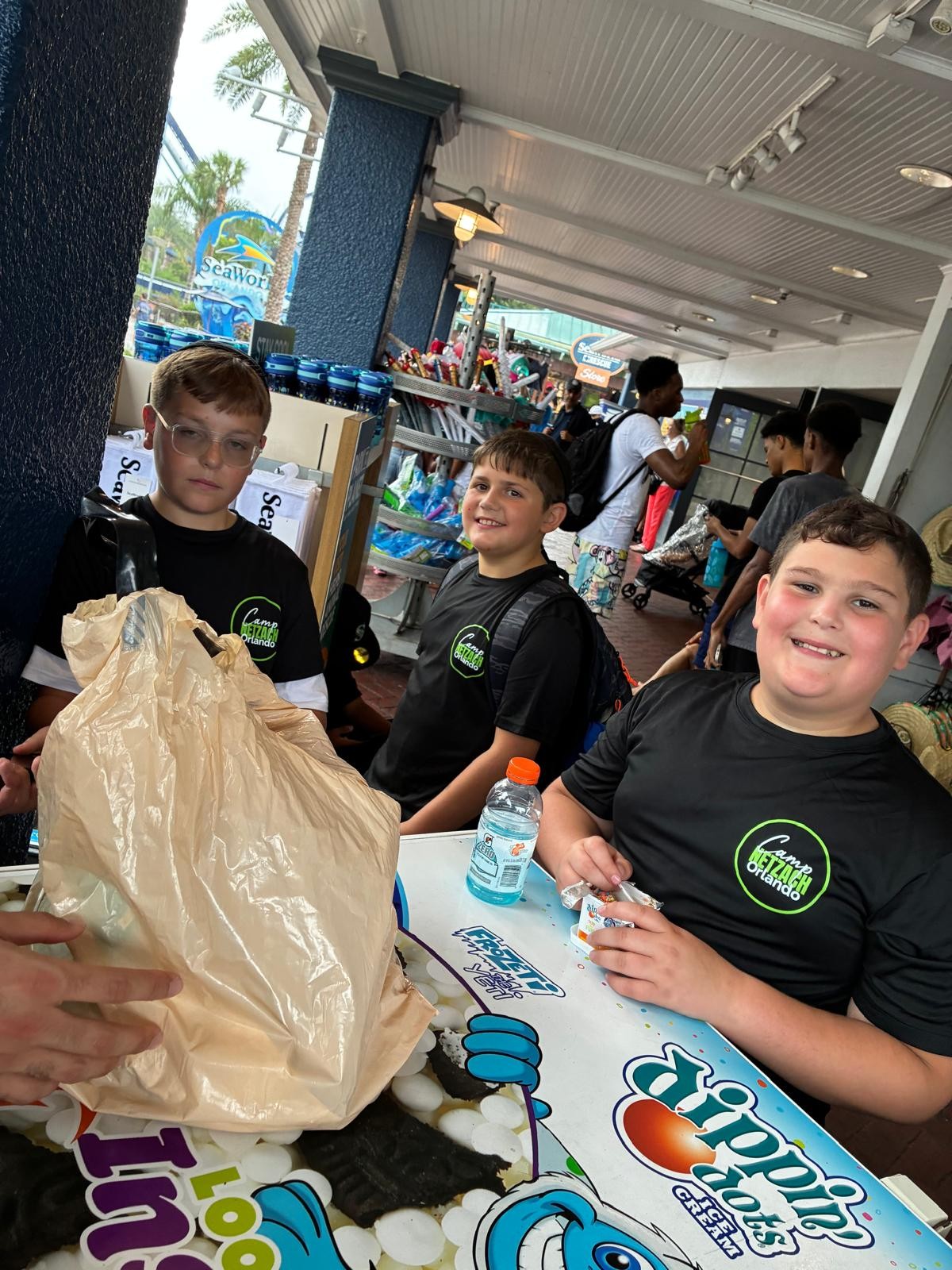 Three campers with ice cream beside a cart at a theme park