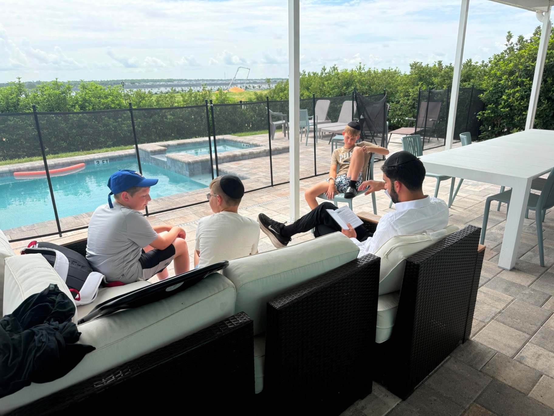 A counselor reading from an open book with three campers on a patio beside the pool