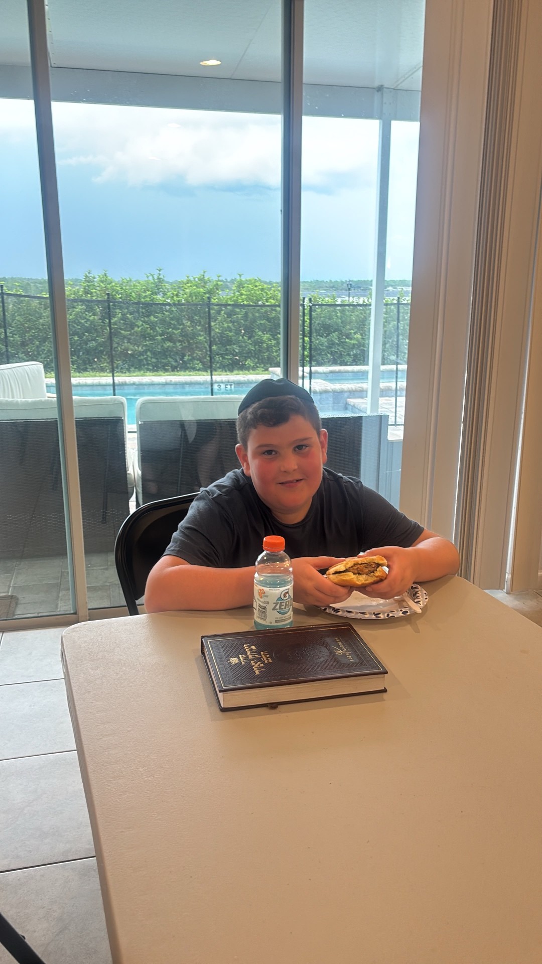 A camper smiling over lunch with a prayer book on the table