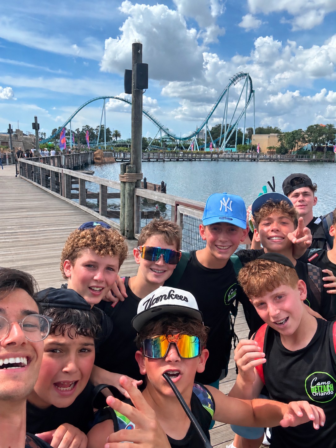 Campers taking a group selfie on a pier with a roller coaster behind them