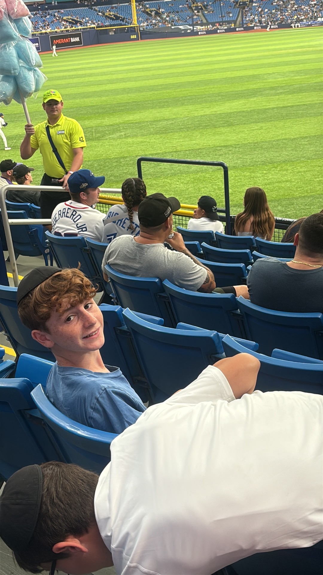 A camper turning to smile at the camera from blue stadium seats at a baseball game