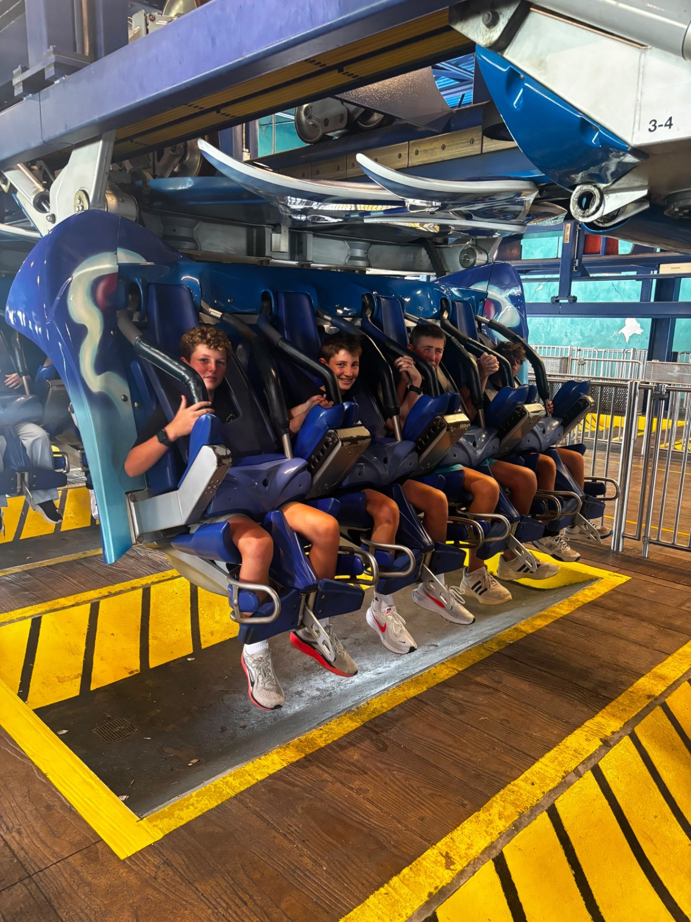 Four campers strapped into a roller coaster train at the station