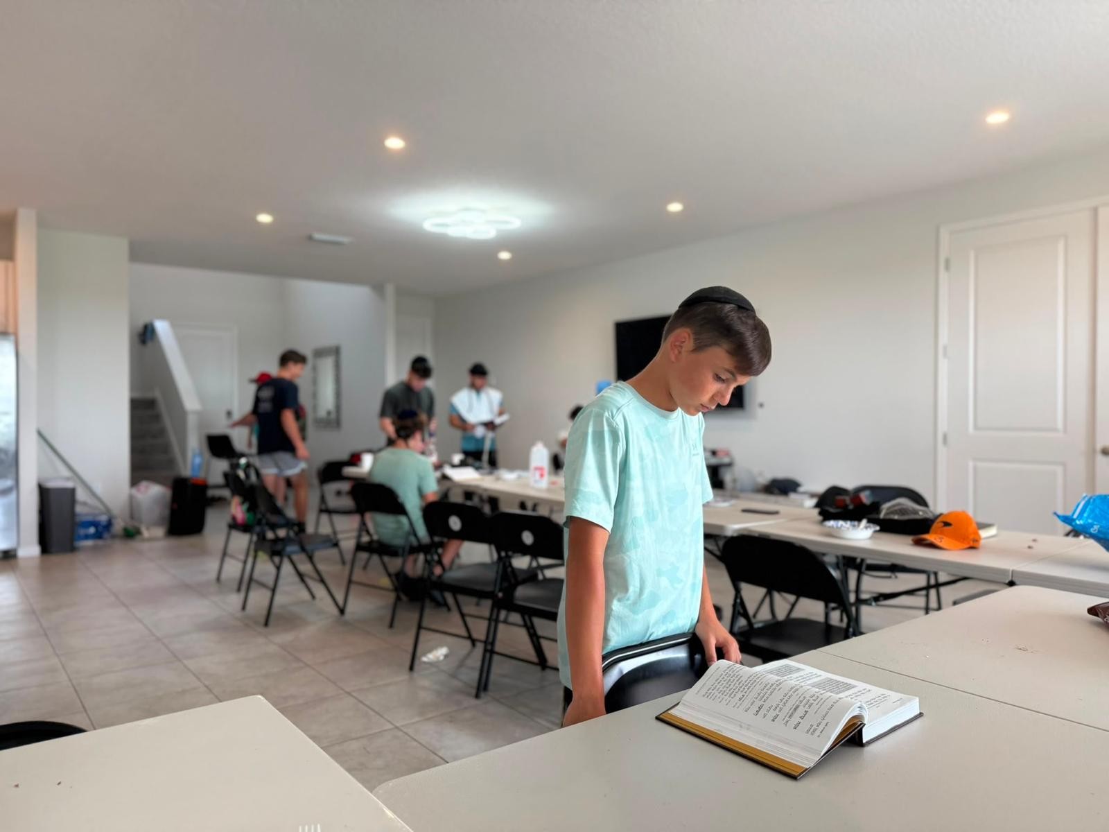 A camper reading from an open prayer book at a table during learning time