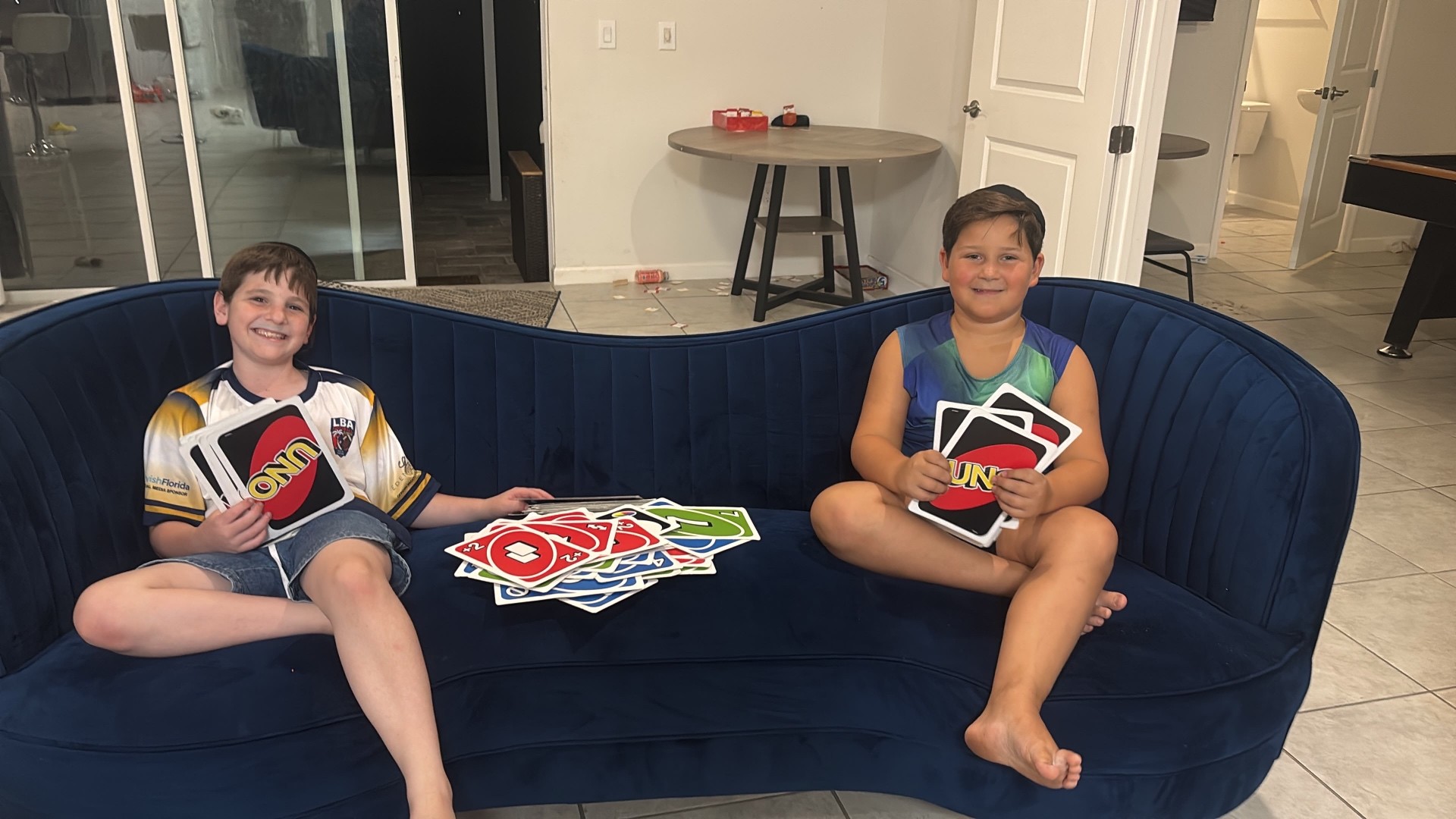 Two campers smiling on a blue sofa holding oversized UNO cards