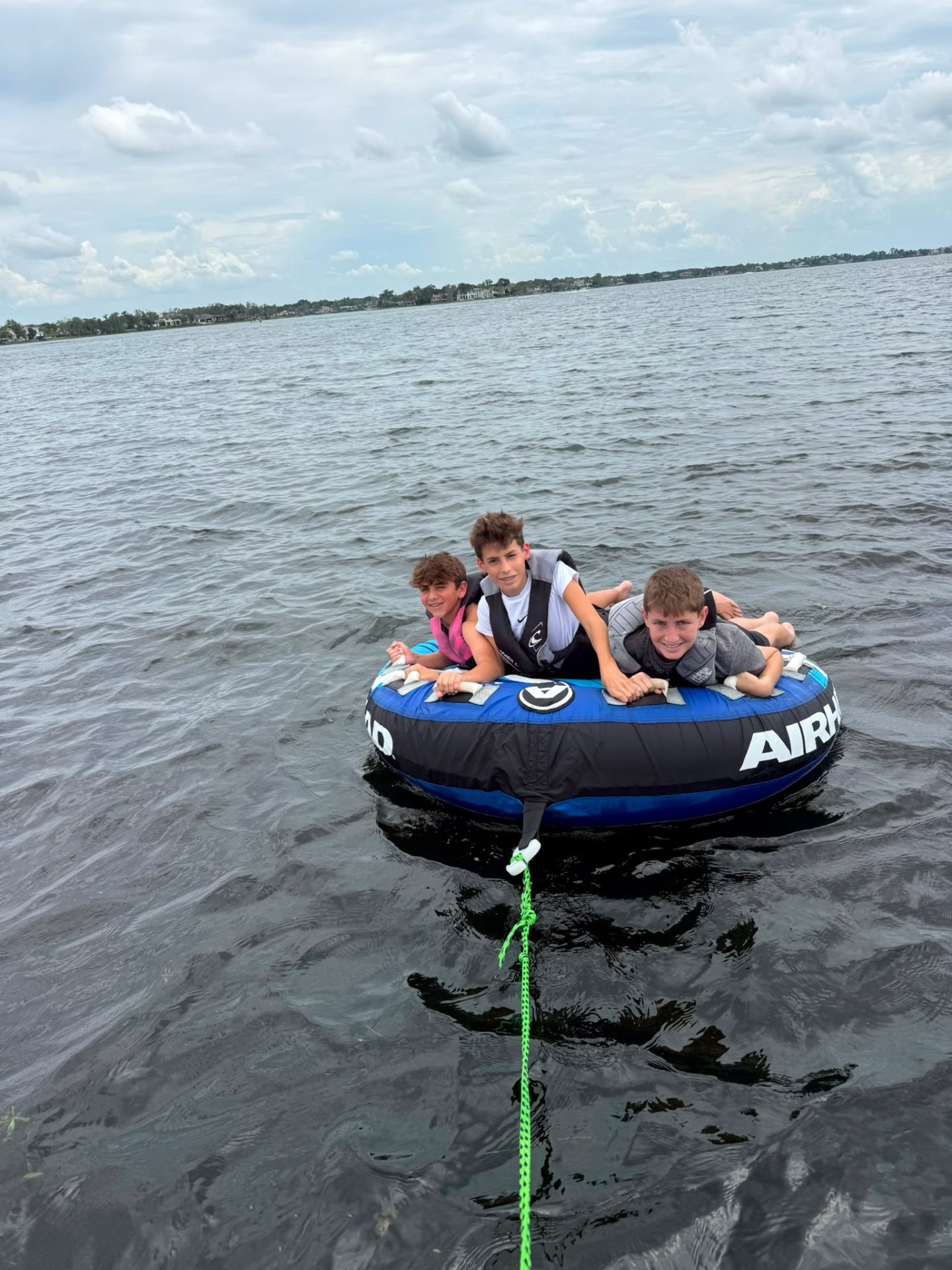 Three campers in life vests riding an inflatable tube across the lake