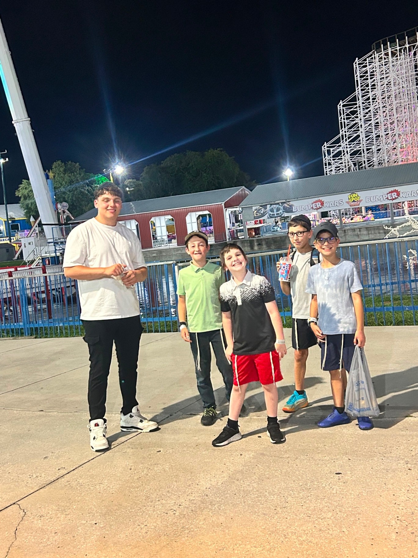 A counselor and four campers posing together at an amusement park at night