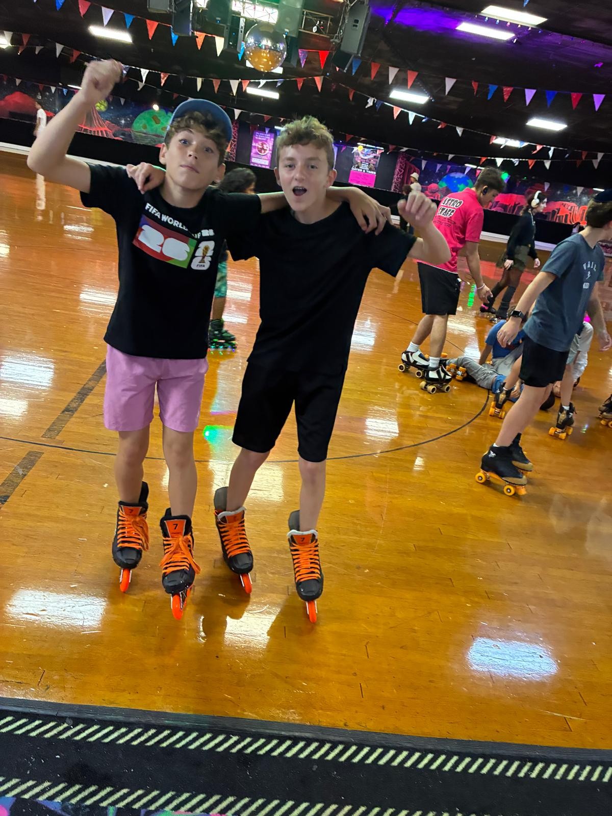 Two campers roller skating together on a colorful indoor rink