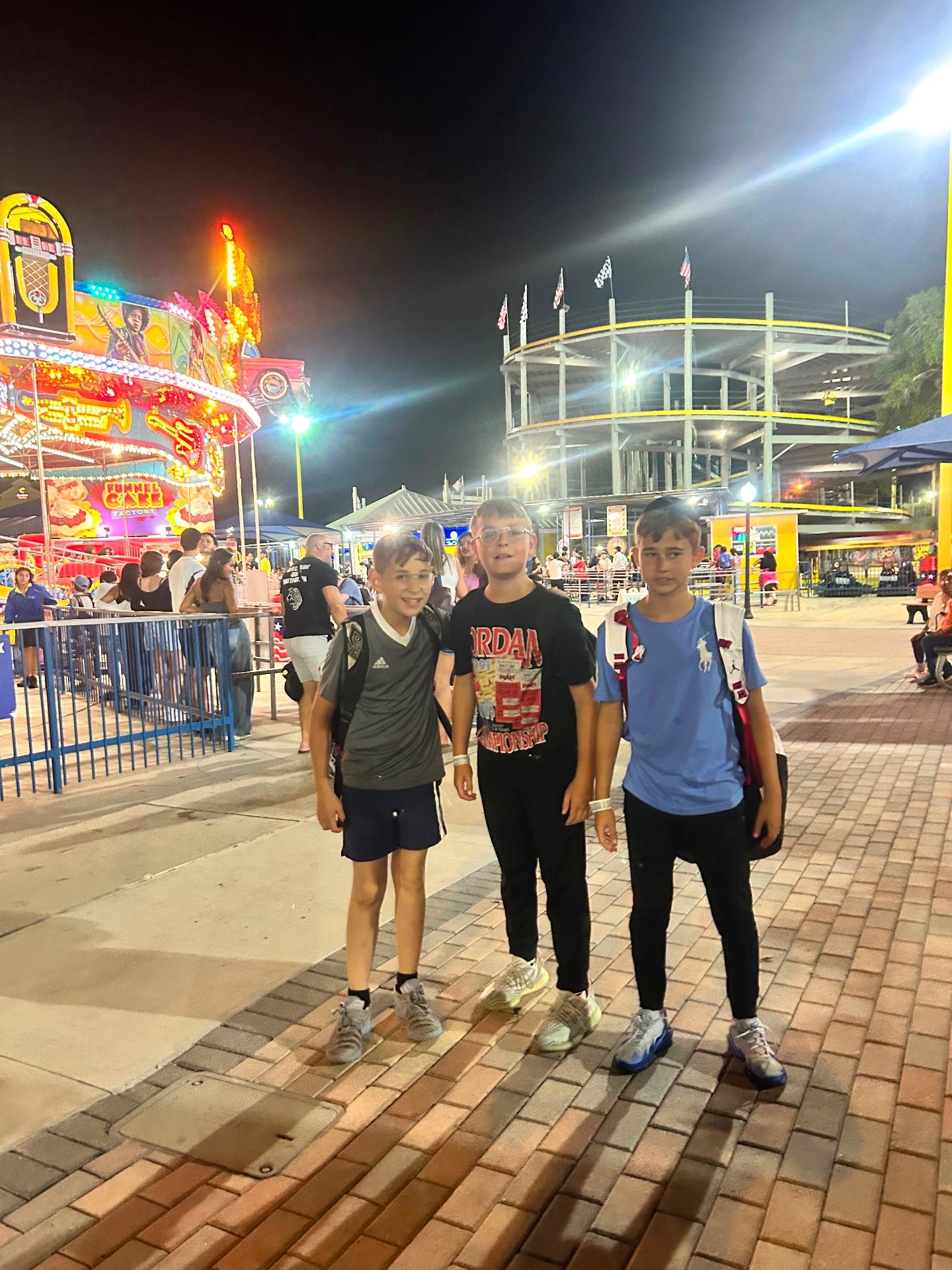 Three campers with backpacks posing together on a brightly lit boardwalk at night