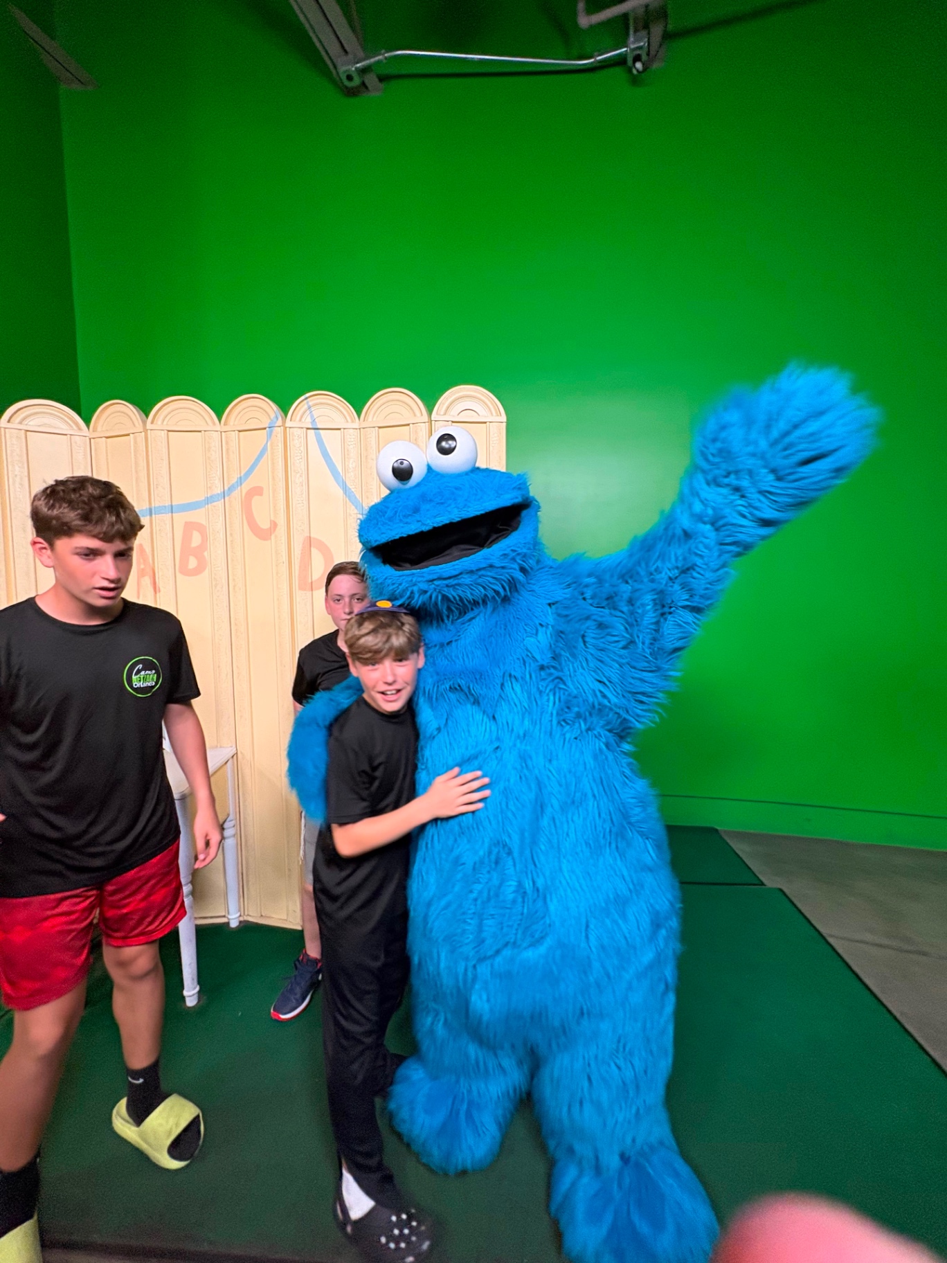 A camper hugging a Cookie Monster character in a green screen studio