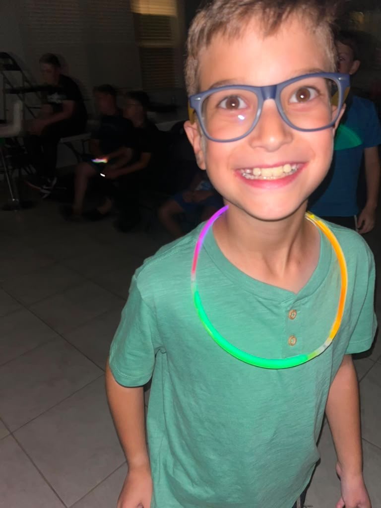 A smiling camper wearing glasses and a glowing neon necklace