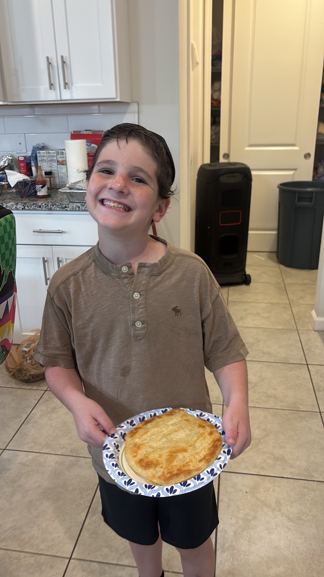 A smiling camper holding a freshly baked pastry on a paper plate in a kitchen