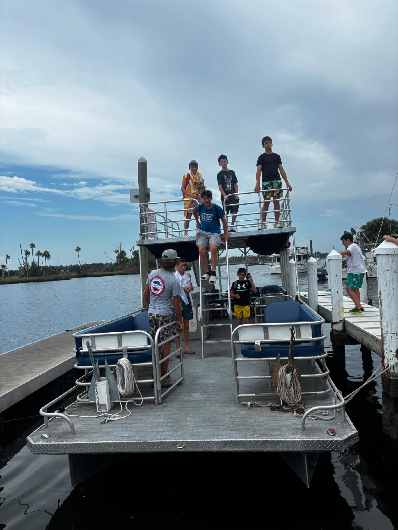 Campers gathered on the decks of a double-decker pontoon boat docked at a marina