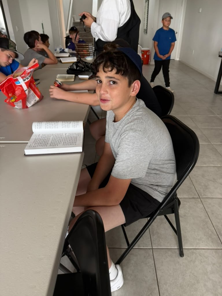 A camper turning to smile at the camera from a learning table with an open prayer book