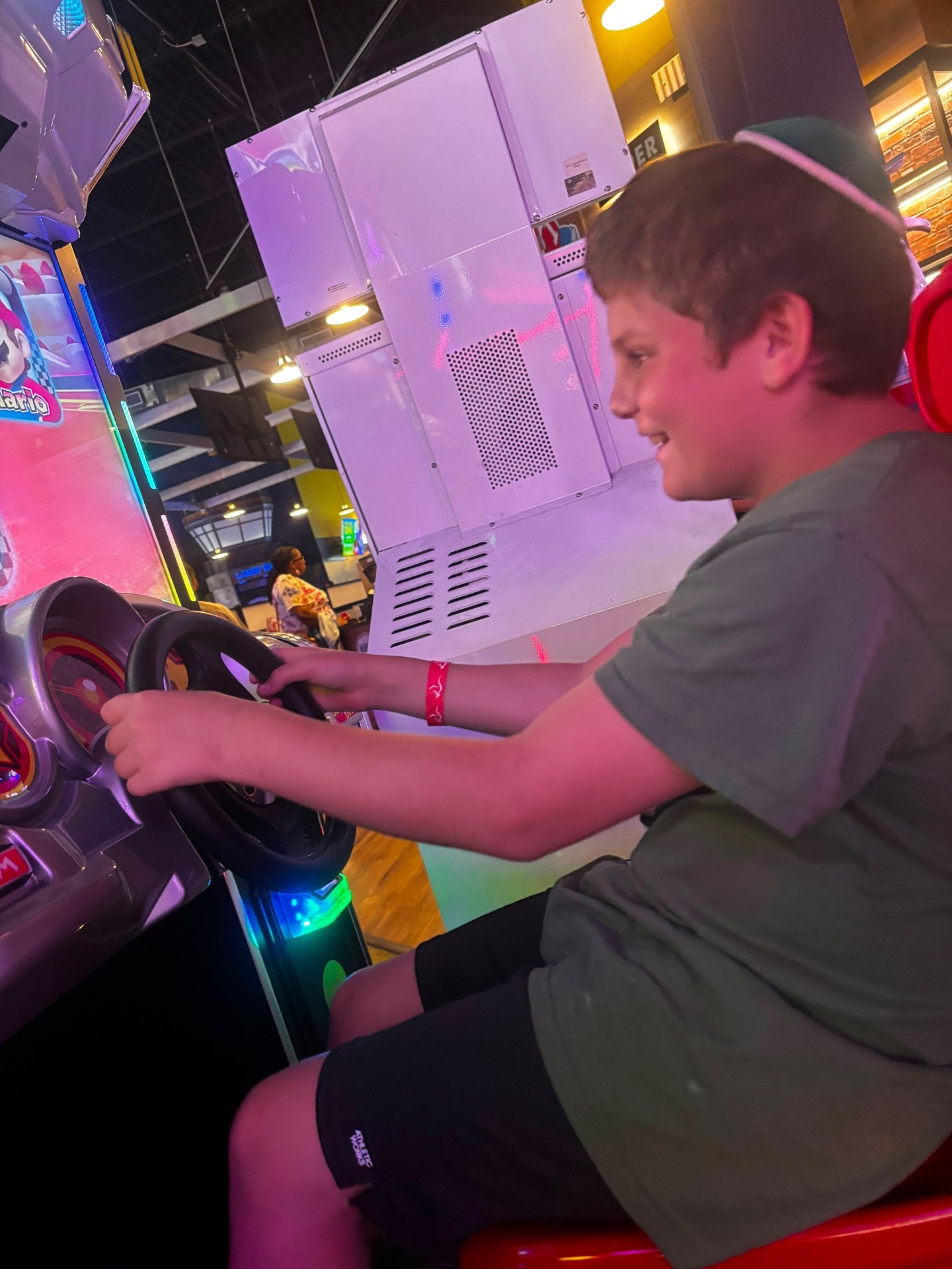 A smiling camper gripping the steering wheel of an arcade racing game
