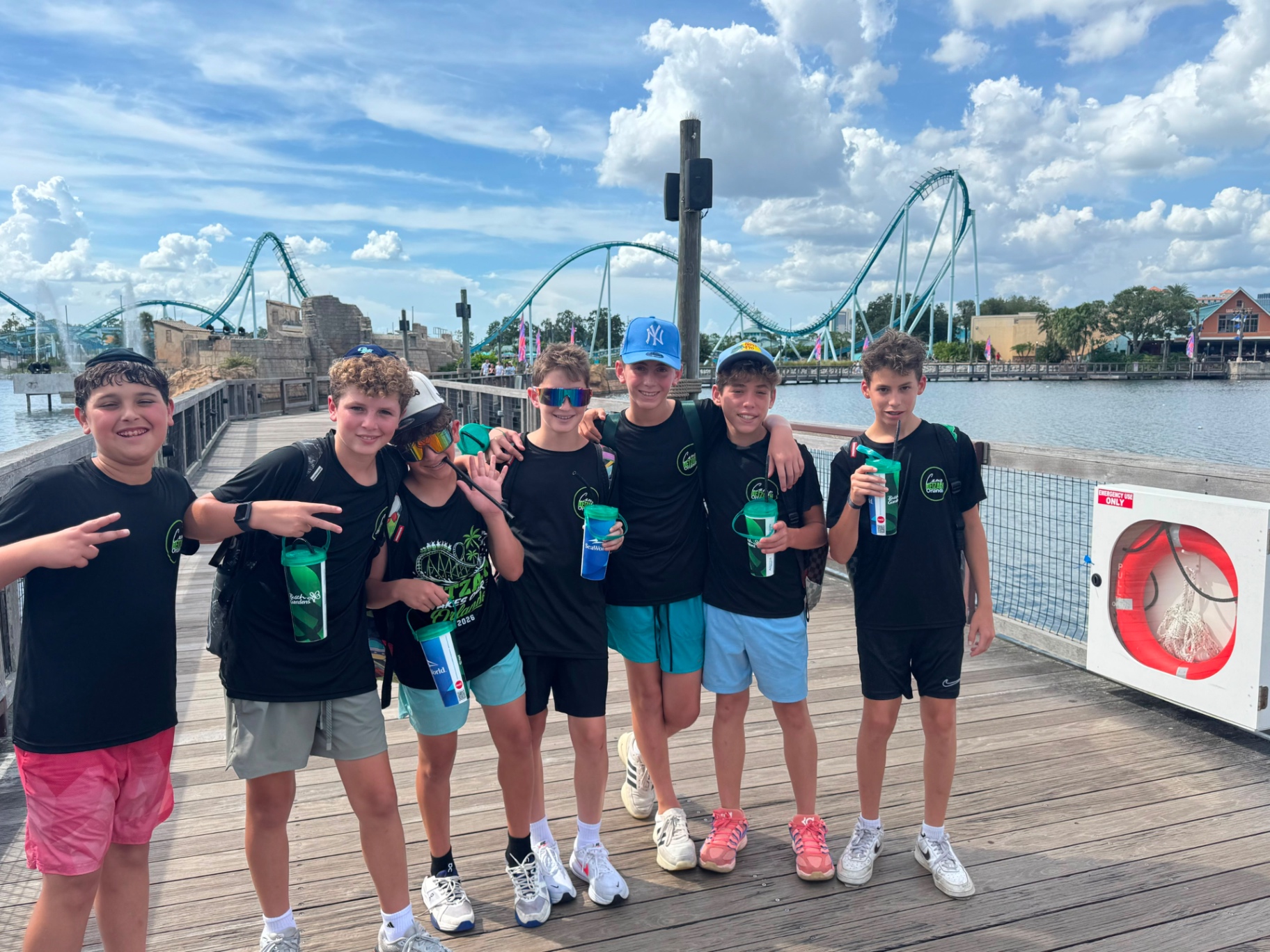 Campers smiling with souvenir cups on a boardwalk in front of a roller coaster