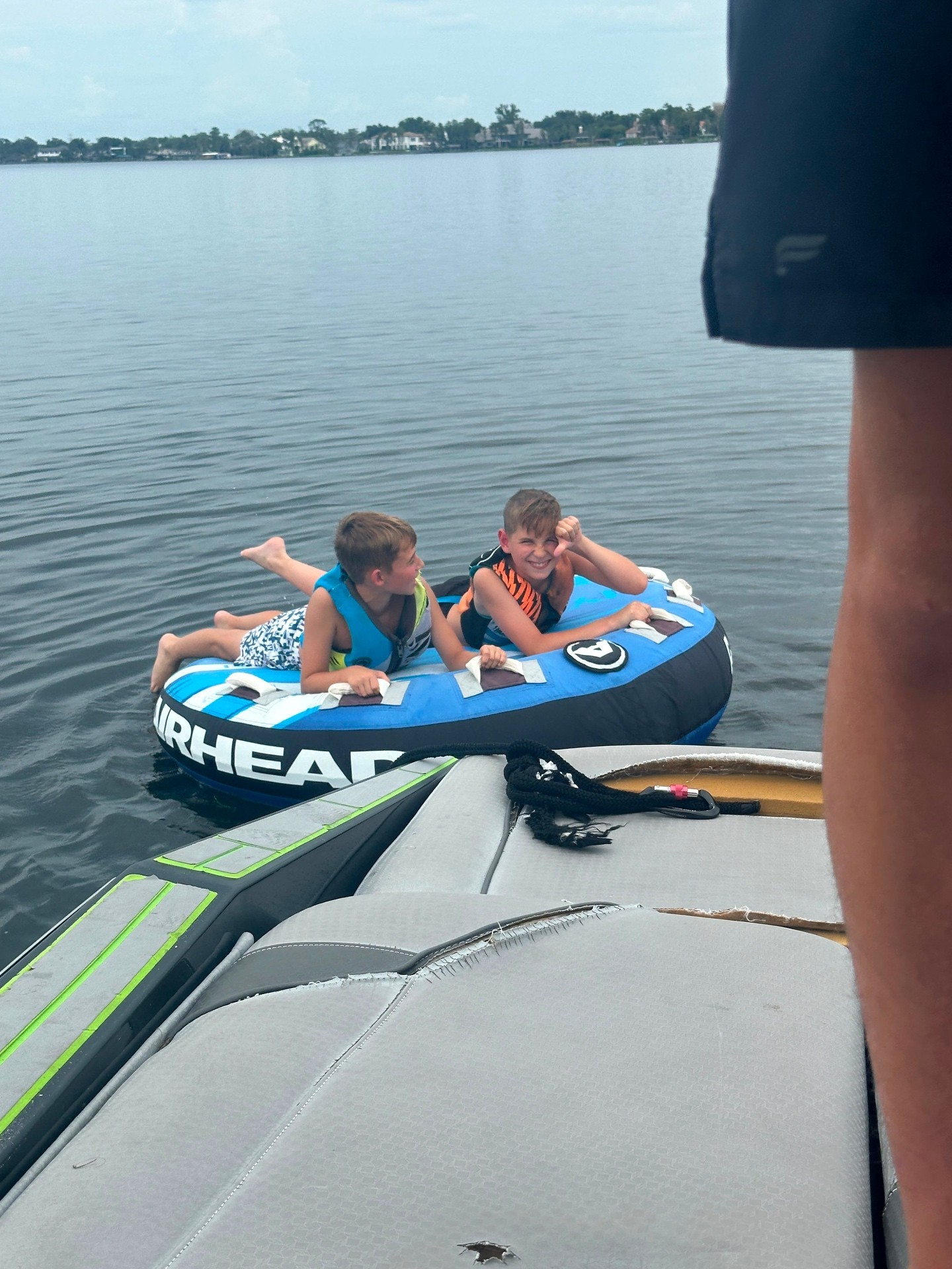Two campers in life vests holding the straps of an inflatable tow tube on the lake