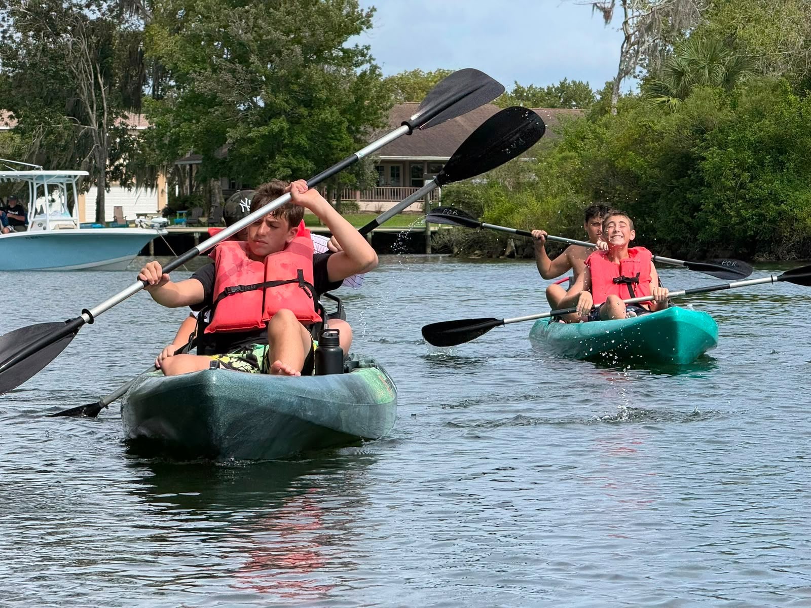 Campers paddling kayaks and splashing water on a sunny canal