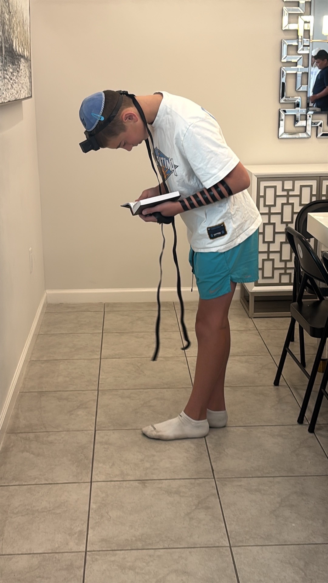 A camper wearing tefillin bowing in prayer while reading from a book