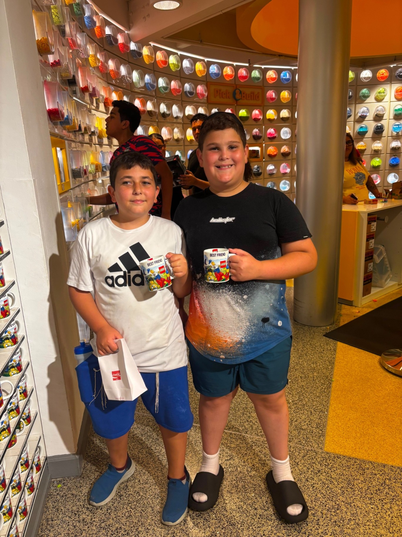 Two campers holding matching best-friend mugs inside a LEGO store