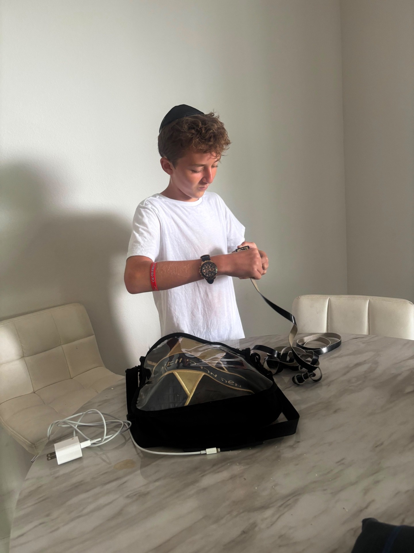A camper wrapping tefillin straps at a marble table