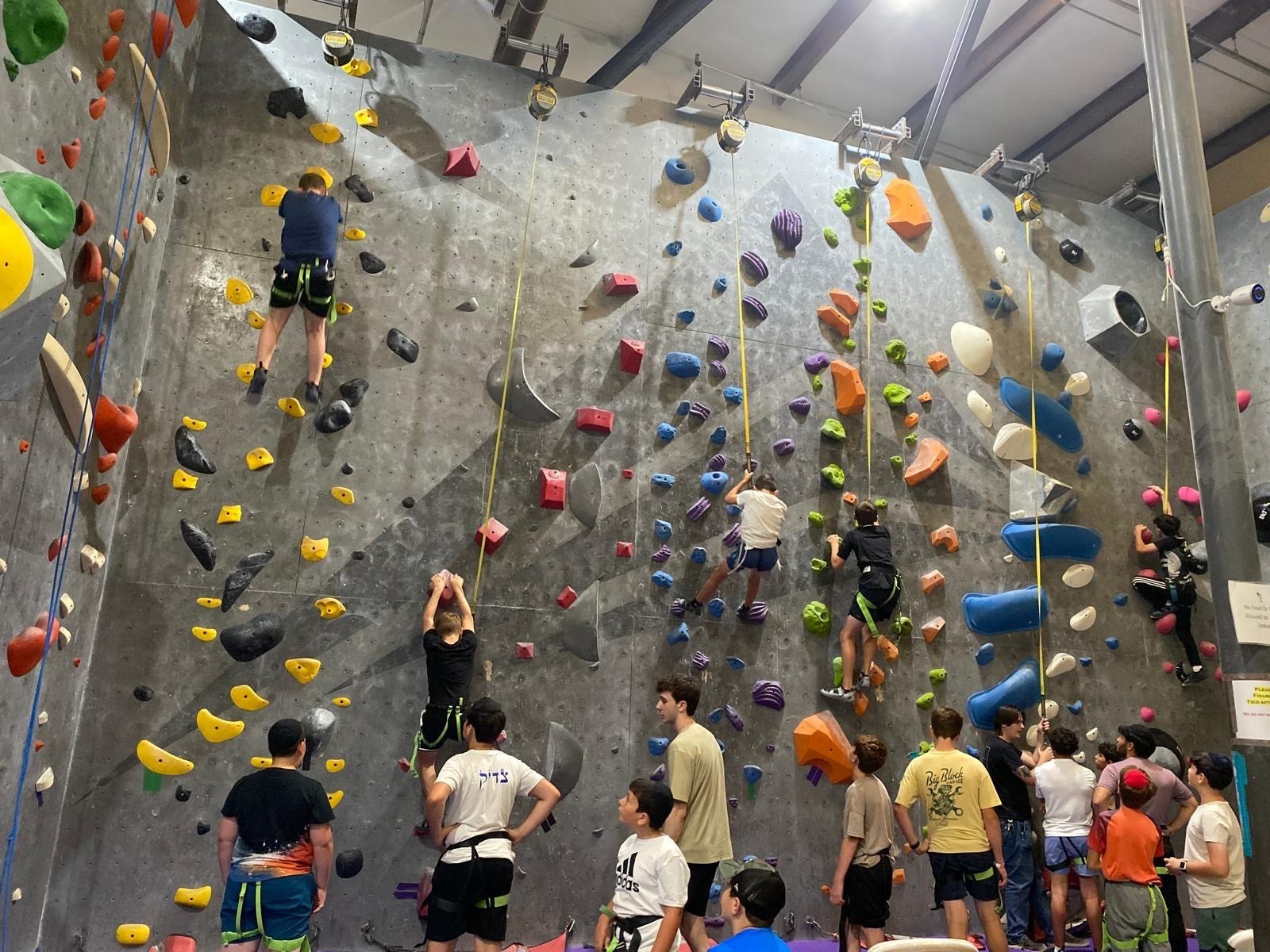 Campers climbing an indoor rock wall while others cheer from below