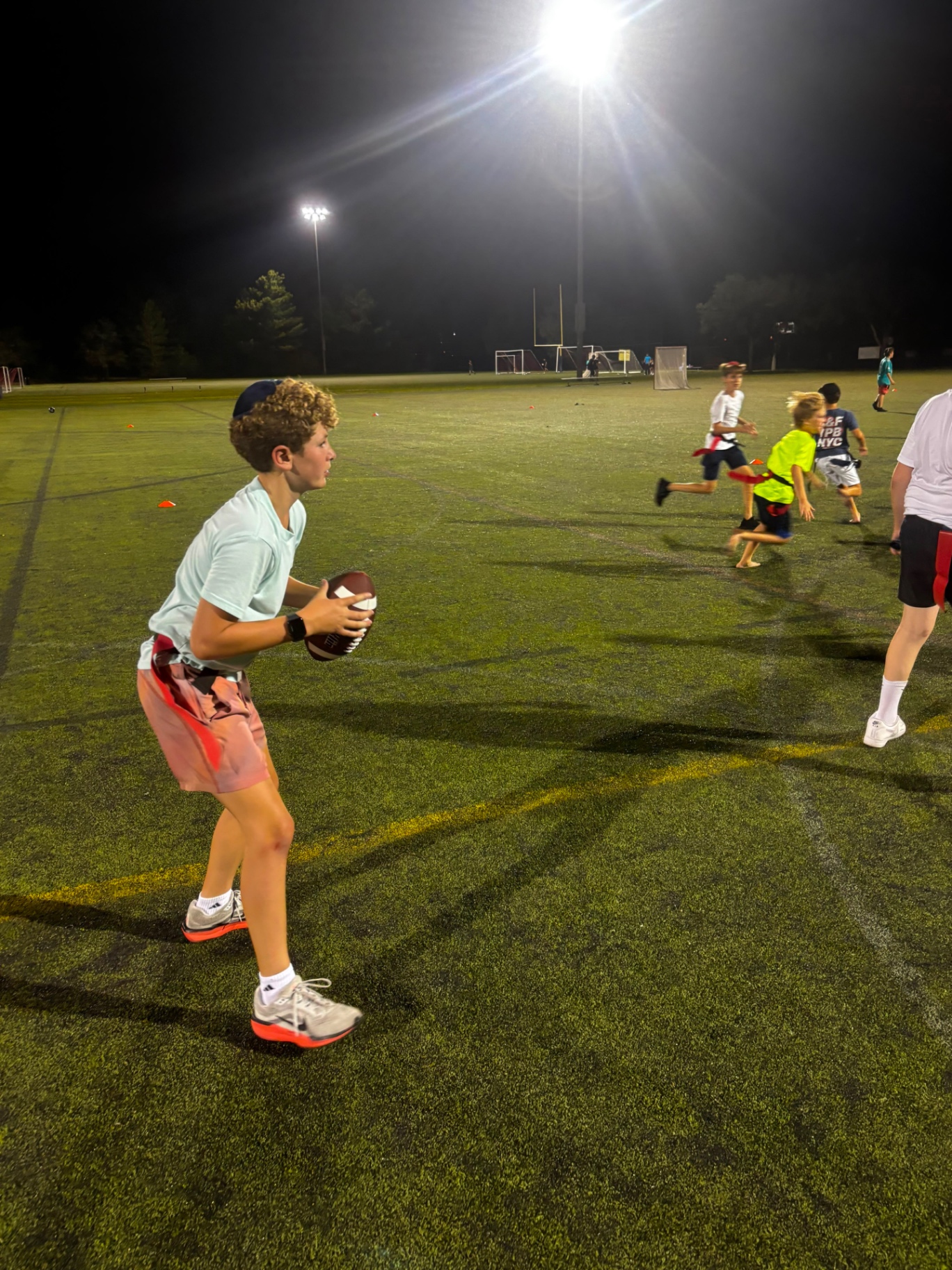A camper holding a football during a night flag football game under stadium lights