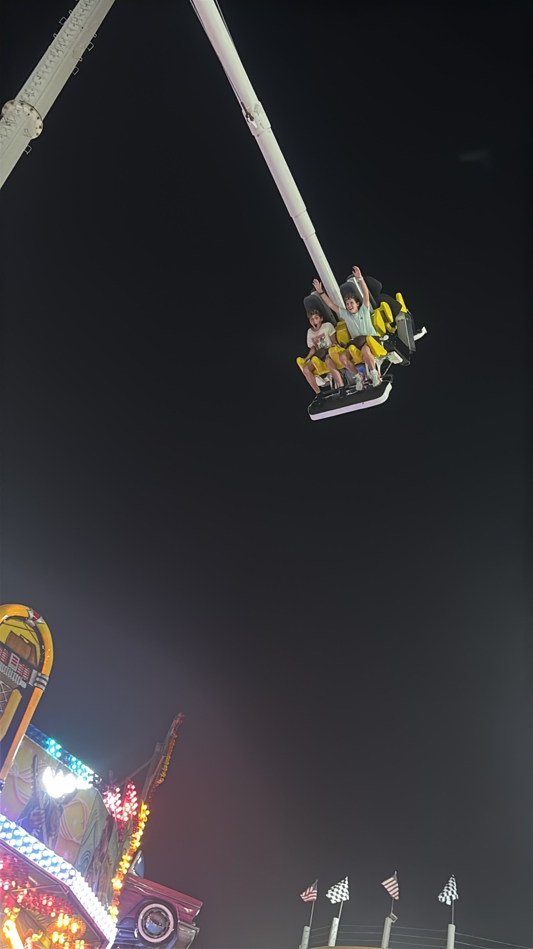 Two campers high in the air on a thrill ride at a lit-up amusement park at night