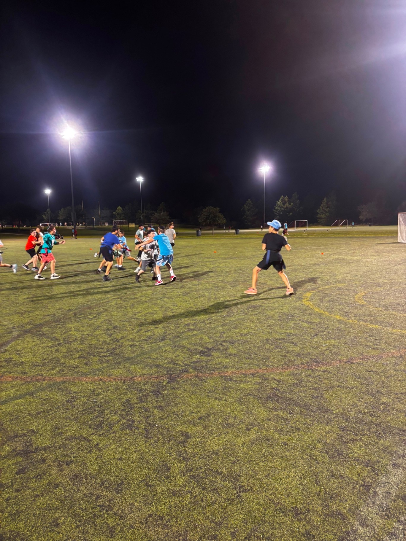 Campers playing a field game at night on a floodlit turf field